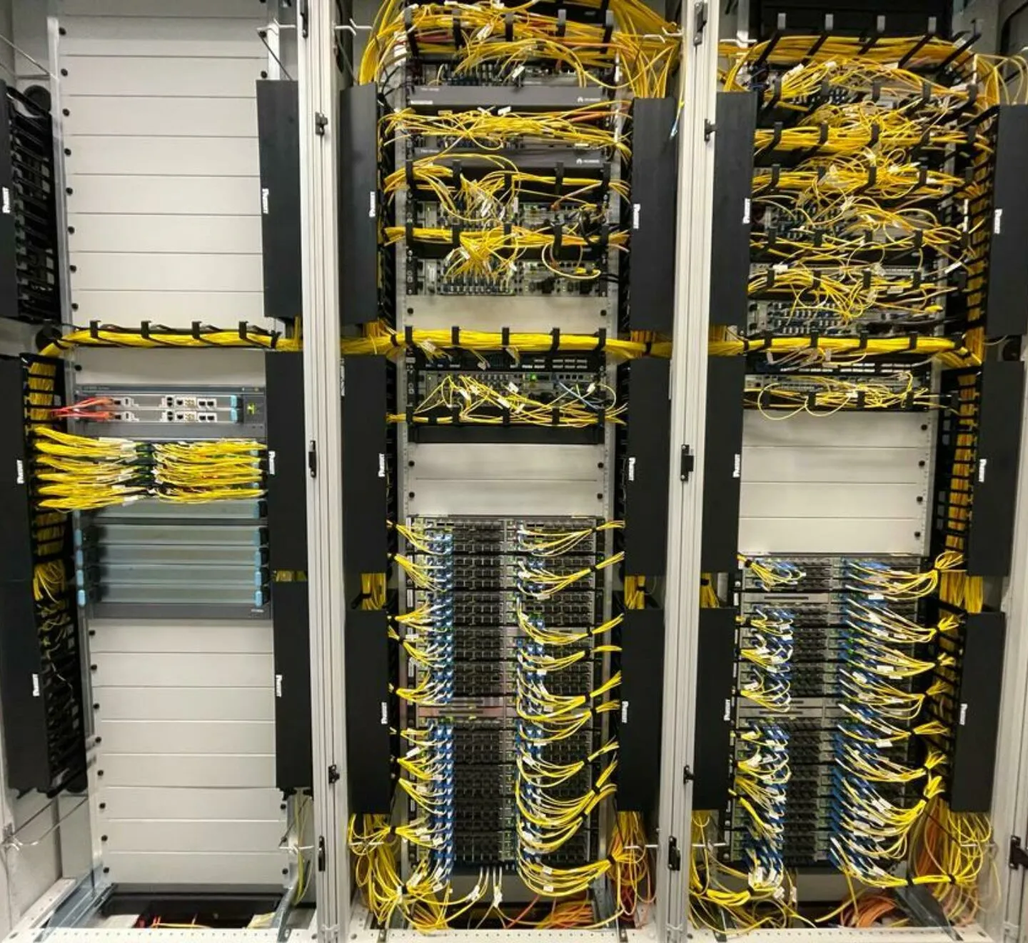 Three racks in a data centre full of network equipment and yellow fibre cables
